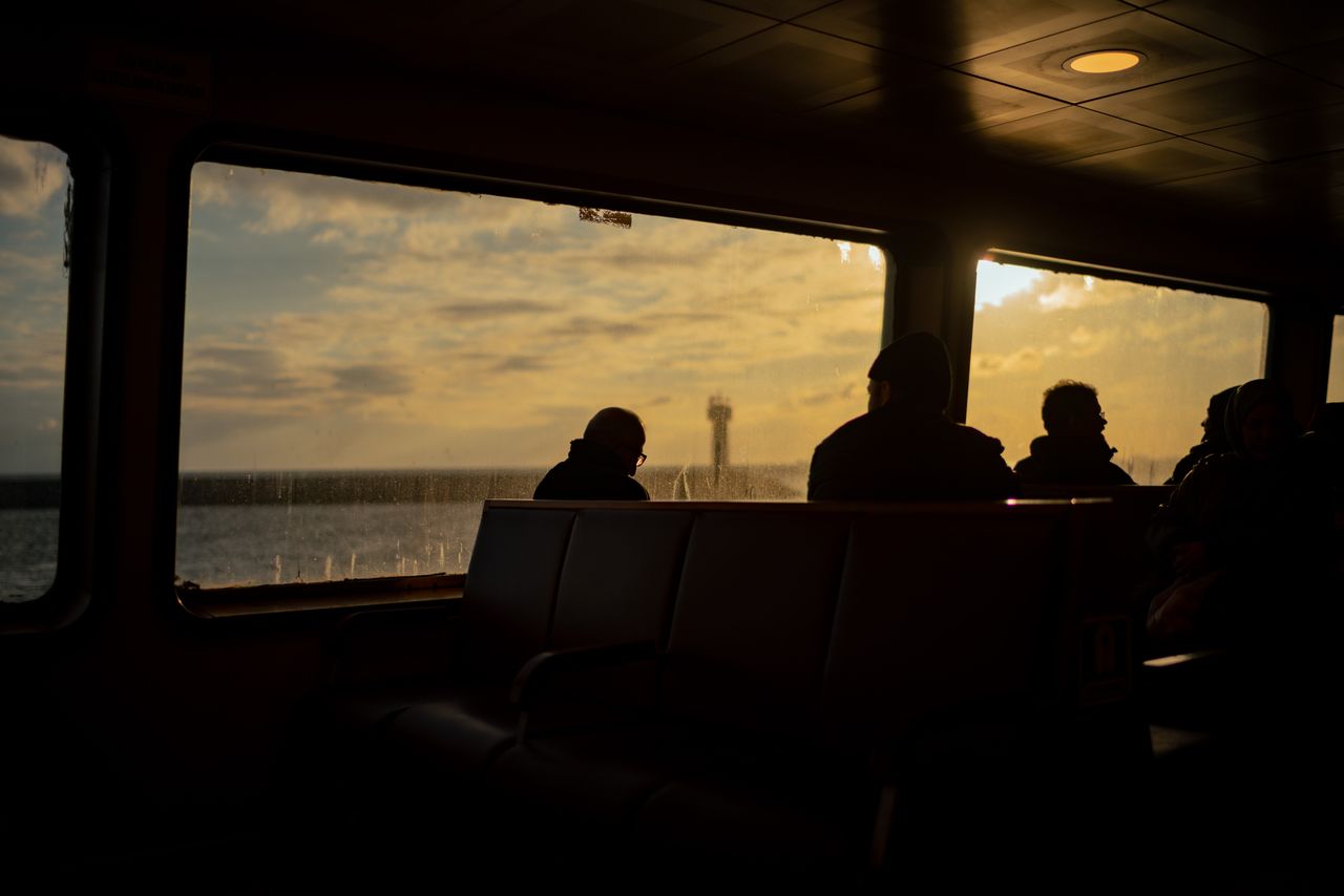 Silhouettes of passengers inside a ferry during sunset, viewing the sea outside.